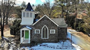 Une petite maison en bois à deux étages, avec une porte verte et une cloche sur le porche.