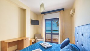 Habitaci ón de hotel con cama, escritorio, silla, televisor y vista al mar a través de un ventanal grande.