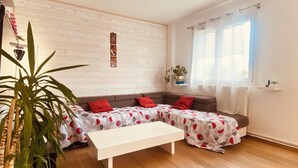 Una sala de estar con un sofá seccional, una mesa de centro blanca y una planta grande.