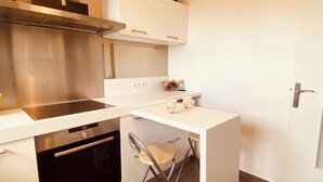 Cocina compacta con extractor de acero inoxidable, horno integrado y una pequeña encimera con cafetera y taza.