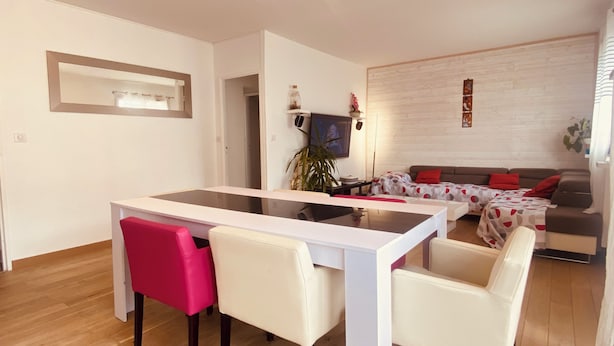 Una sala de estar moderna con un sofá blanco, una mesa de comedor y una silla rojo brillante.