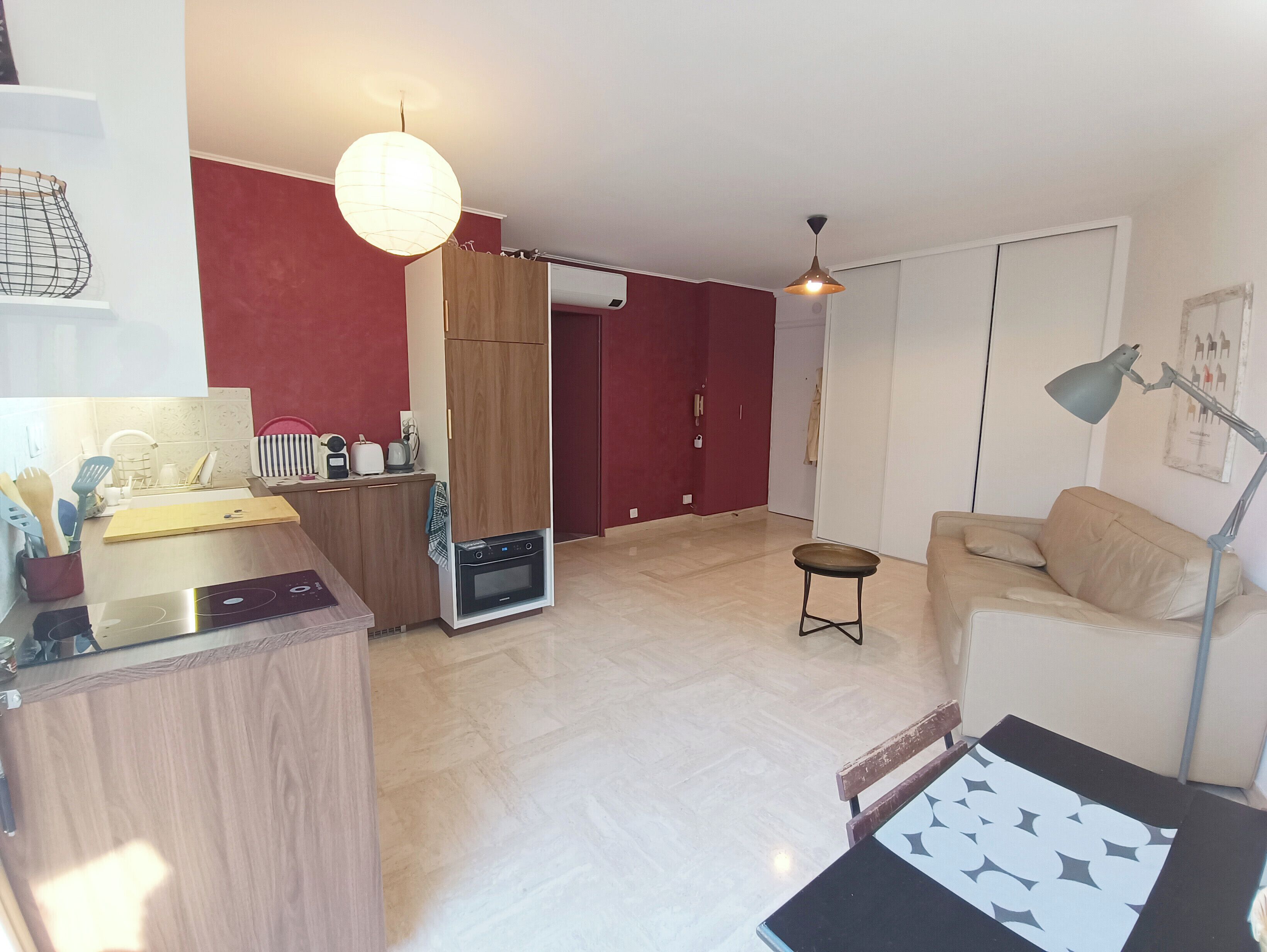 A modern living room with a sofa, a coffee table, a dining area with a kitchen counter, and a built-in oven.