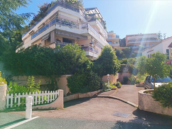 A multi-story residential building with balconies, a gated entrance, and surrounding greenery.