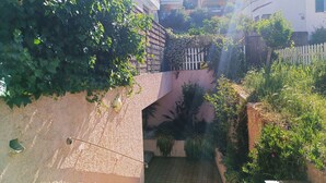 Uma passagem estreita com caminho de azulejos, rodeada por vegetação exuberante e edifícios com varandas.