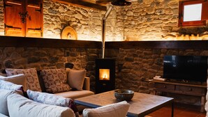 A cozy living room with a stone wall, a fireplace, a sofa, a coffee table, and a television. - El Molino del Cidacos (Arnedillo)