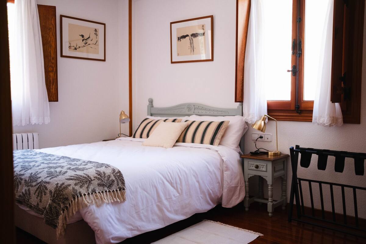 A bedroom with a bed, bedside table, lamp, and a crib.