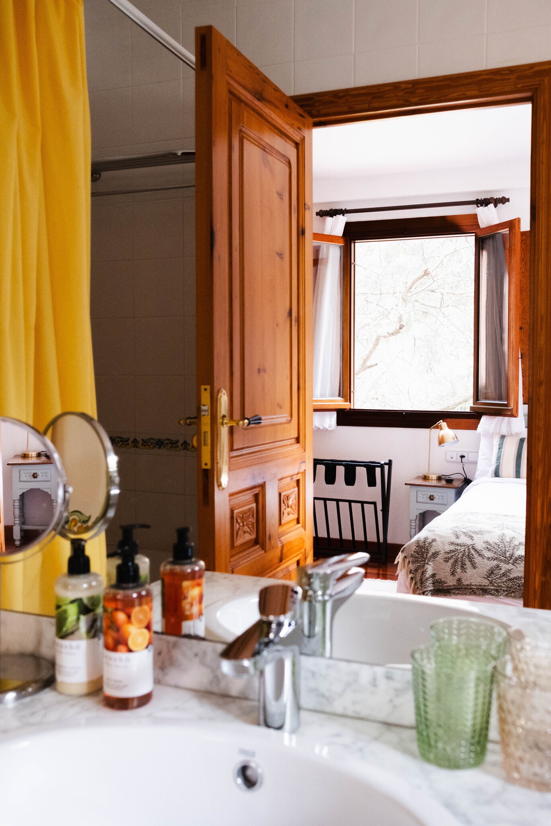 A bathroom with a wooden door, a mirror, a sink, and toiletries.