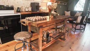 Une cuisine avec un îlot central en bois, des tabourets, une machine à café et un vase à fleurs.