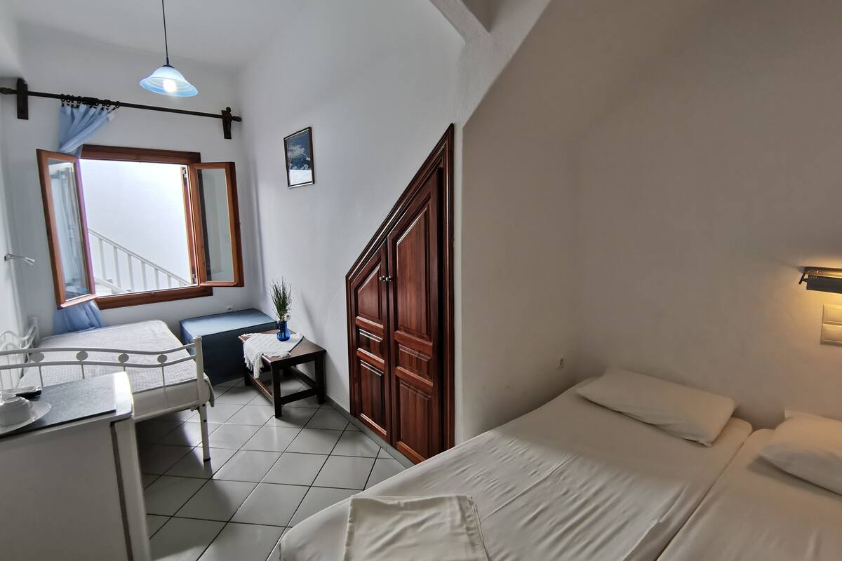 Un dormitorio con cama, escritorio, silla, armario, ventana con cortinas y lámpara colgante.