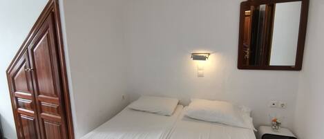 A bedroom with a bed, a nightstand, a mirror, and a wooden door.