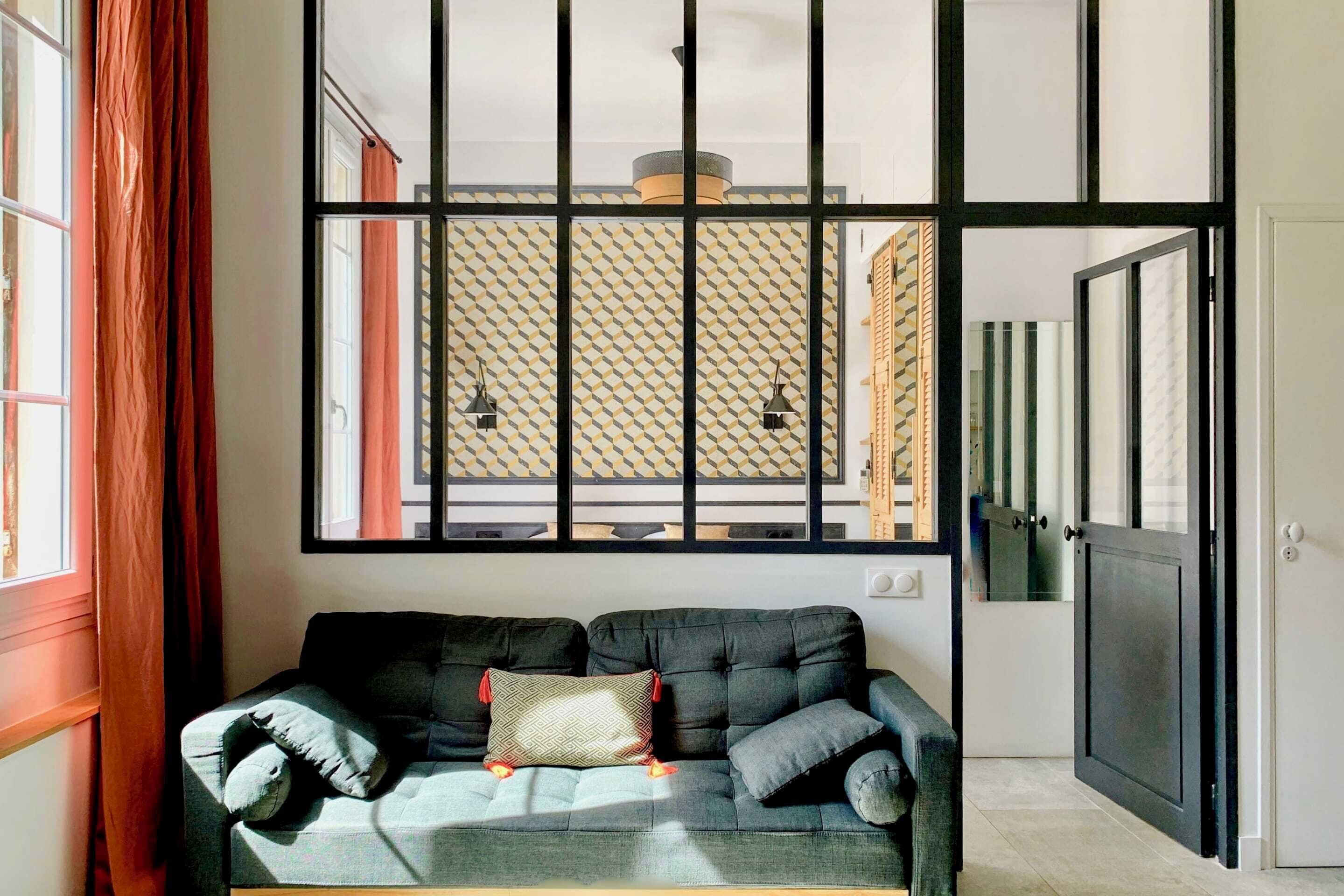 A modern living room with a sofa, a patterned wall, and a large window.