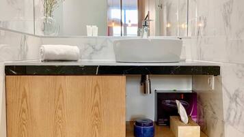 A modern bathroom with a marble sink, wooden vanity, and a mirror reflecting a door and window.