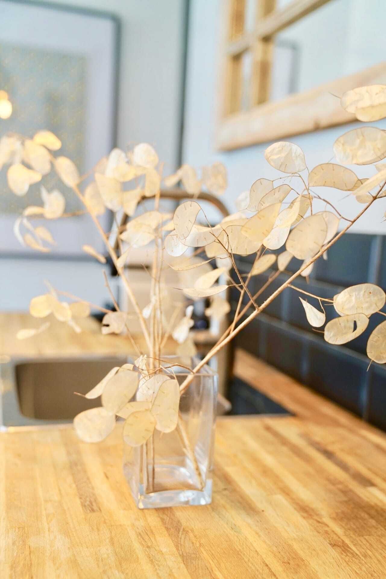 A clear glass vase with dried leaves on a wooden table.