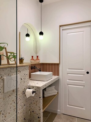 Ein Badezimmer mit weißem Waschbecken, zwei Pendelleuchten, einem Spiegel und einer Tür mit Griff.
