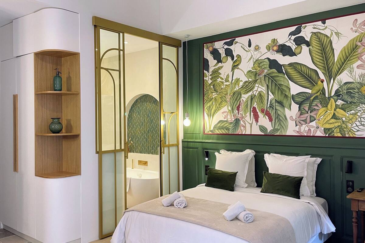 Ein Schlafzimmer mit einem Bett, einem grünen Kopfteil, einer Wand mit einem botanischen Druck und einer Holzkammer mit Dekorationen.