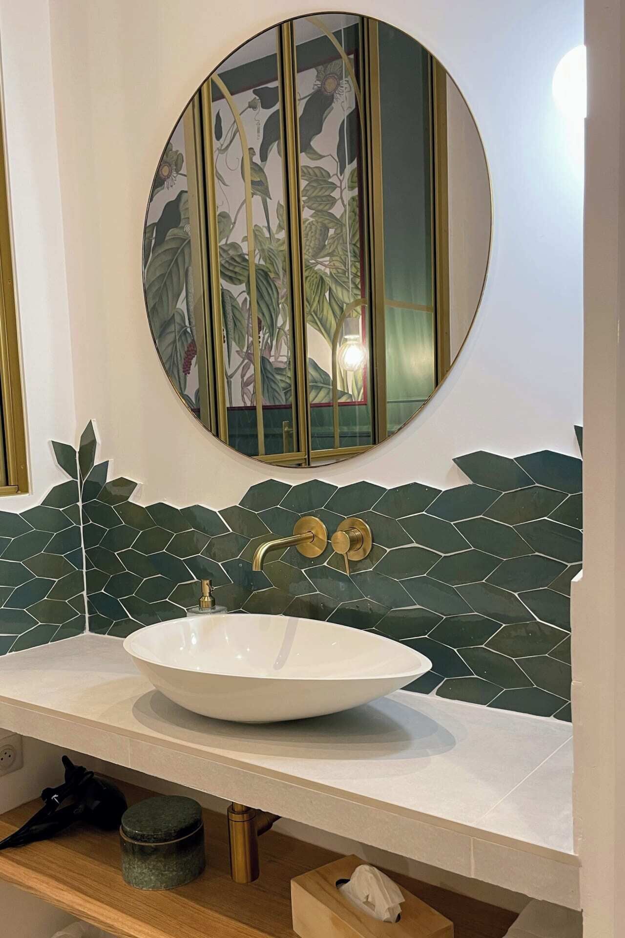 A bathroom with a round mirror, a white sink, and a green leaf-patterned backsplash.