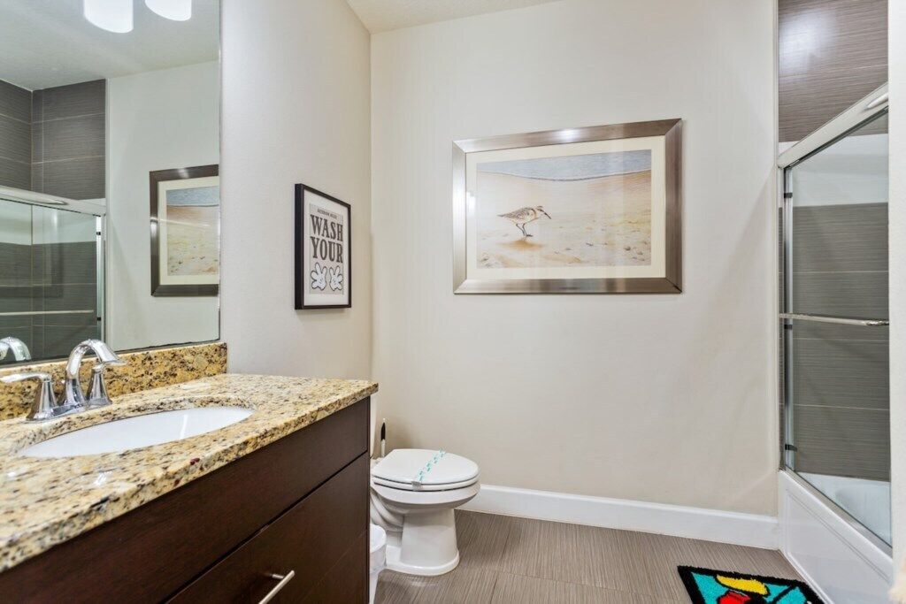 A modern bathroom with a granite countertop sink, a toilet, and a framed artwork on the wall.