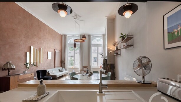 A modern kitchen with a central island, pendant lighting, and a dining area with a round table and chairs. - Bel Appartement de 110m2 Dans un Hôtel Particulier du Xviiie Siècle (Salins-les-Bains)