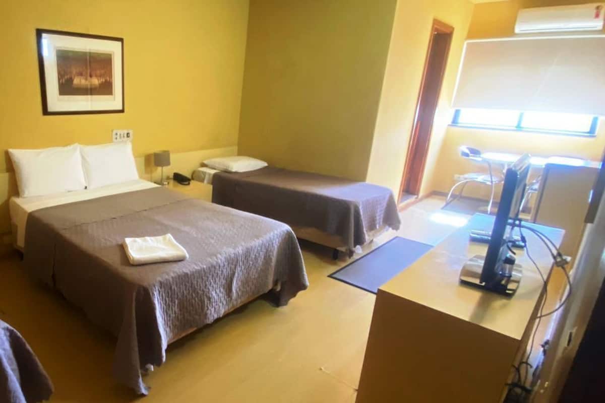 A hotel room with two beds, a desk with a computer, and a window with blinds.