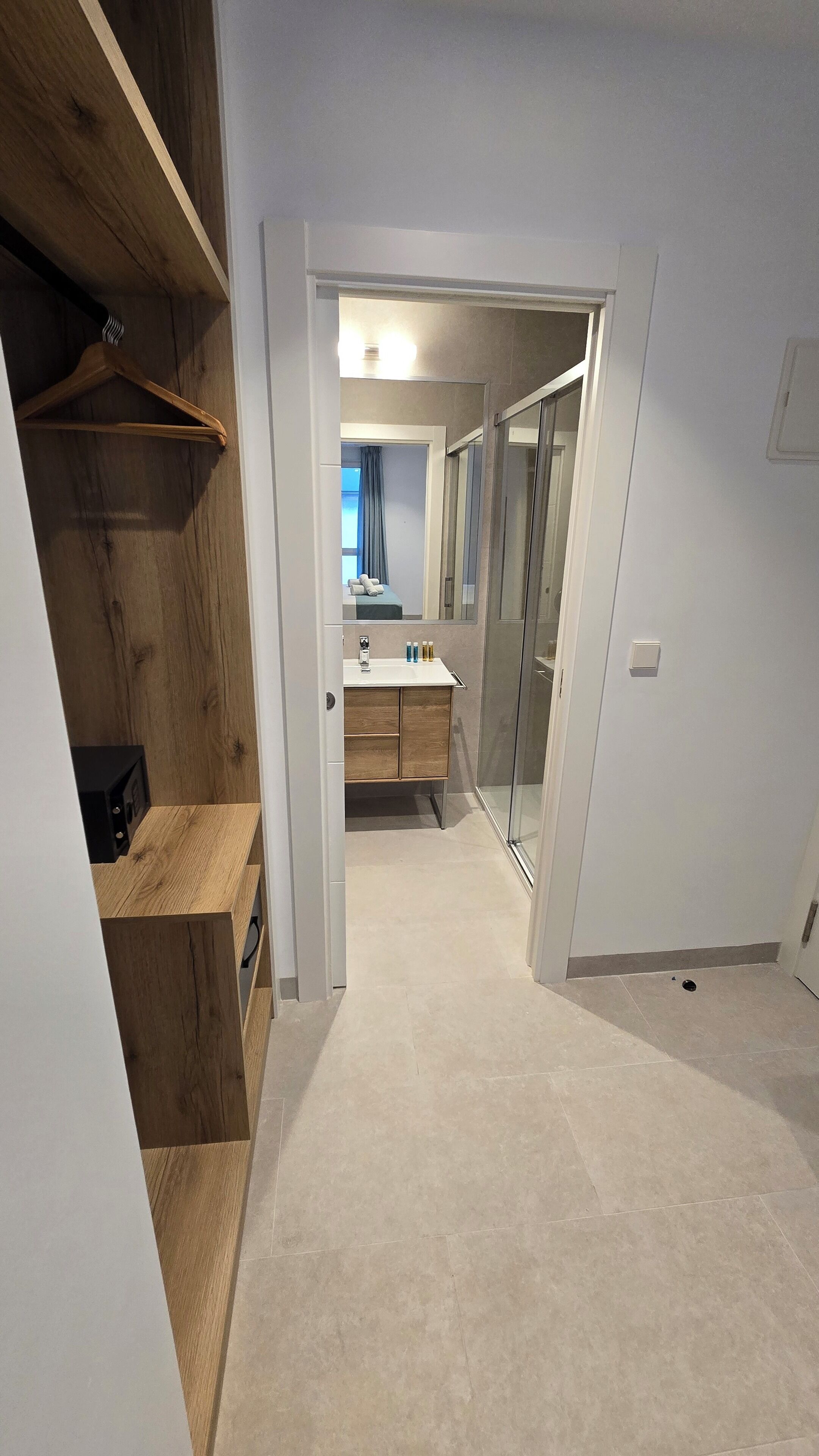 A narrow hallway leading to a bathroom with a wooden vanity, a mirror, and a shower area.