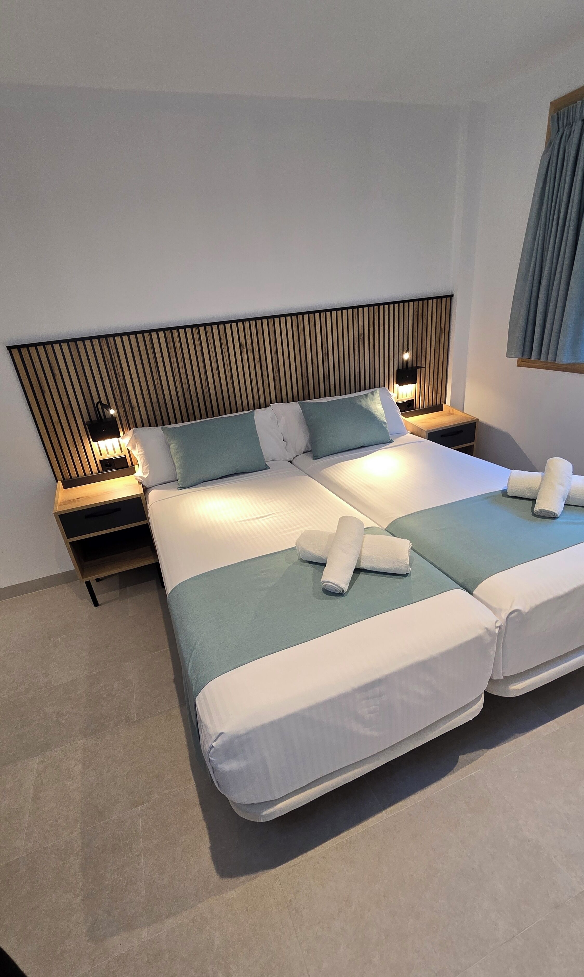 A double bed with a wooden headboard, two bedside tables with lamps, and a blue accent pillow.