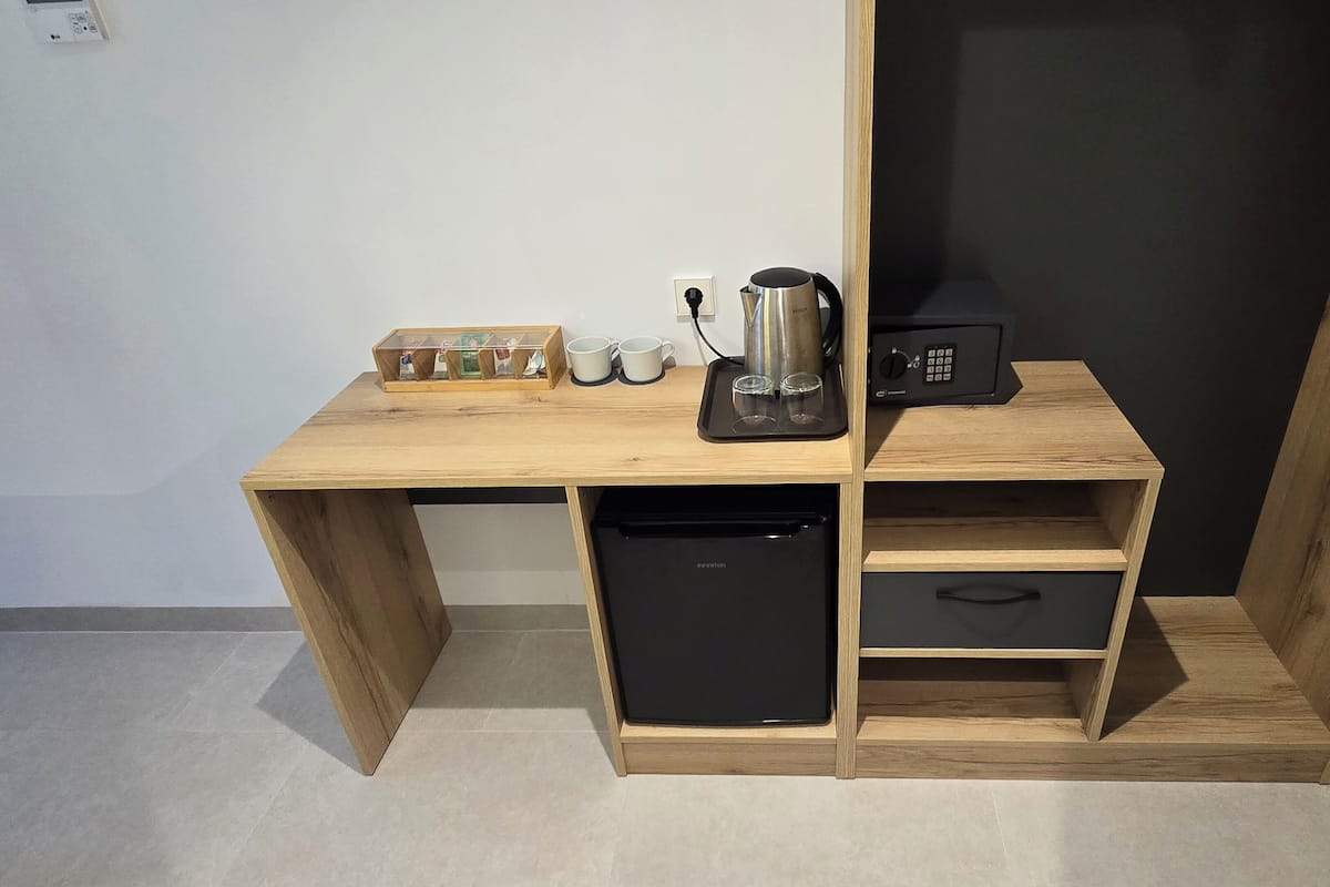 Una kitchenette compacta con cafetera integrada, un refrigerador pequeño y una repisa con bolsitas de té.