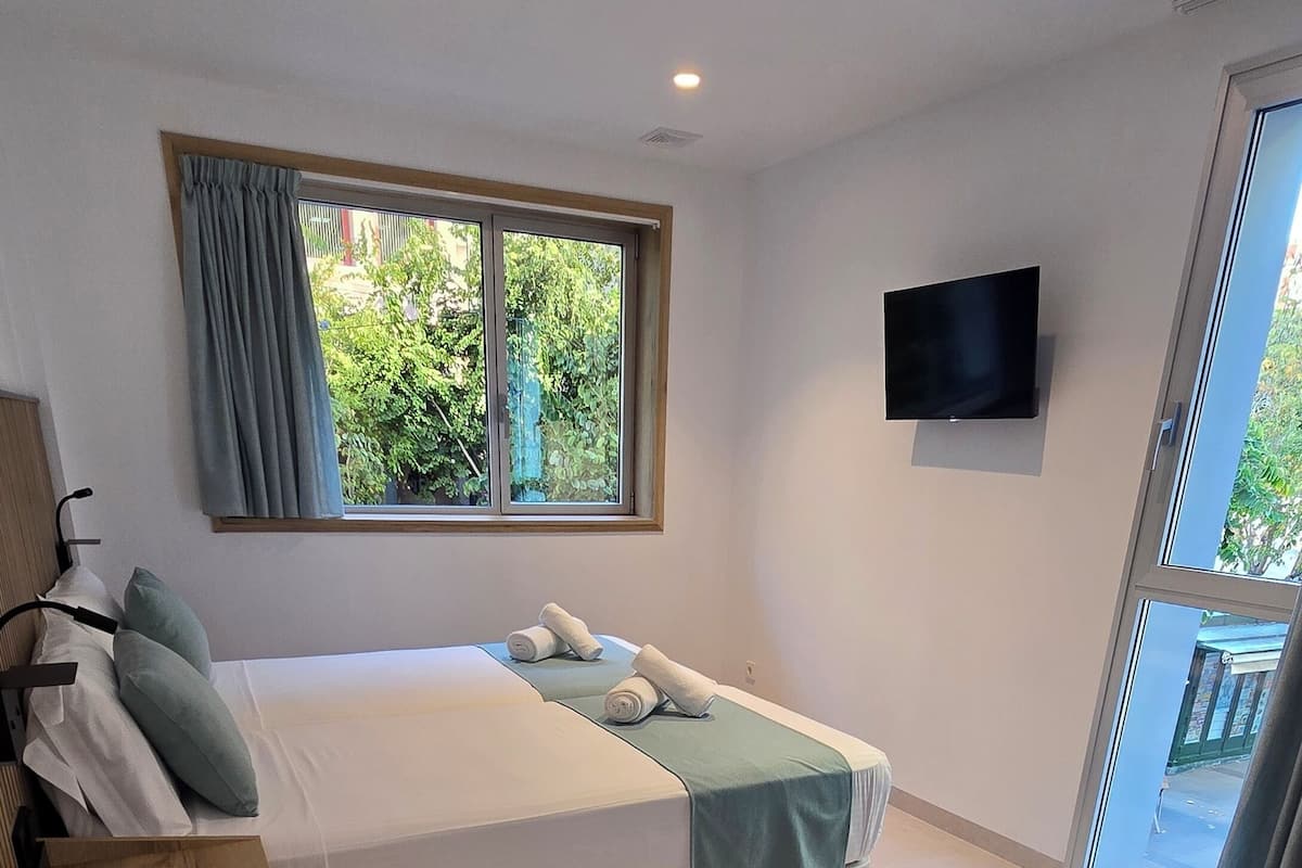Un dormitorio moderno con cama, televisor y ventana con cortinas.
