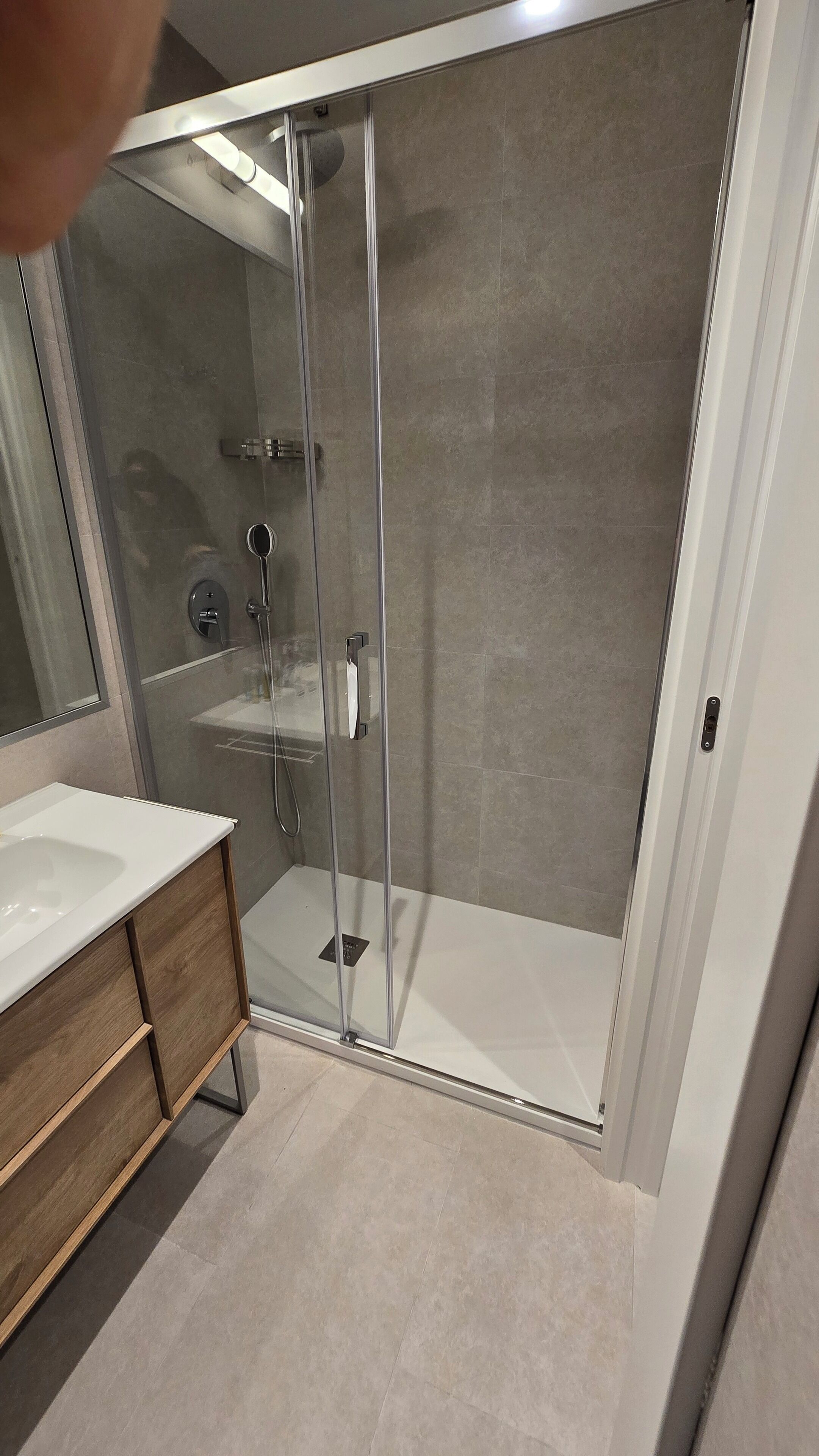 A modern bathroom with a glass-enclosed shower, a white sink, and a wooden vanity.