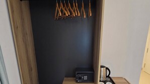 Ein Holzschrank mit einem schwarzen Tresor, einer kleinen Ablagefläche mit Gegenständen und einer Kleiderstange.