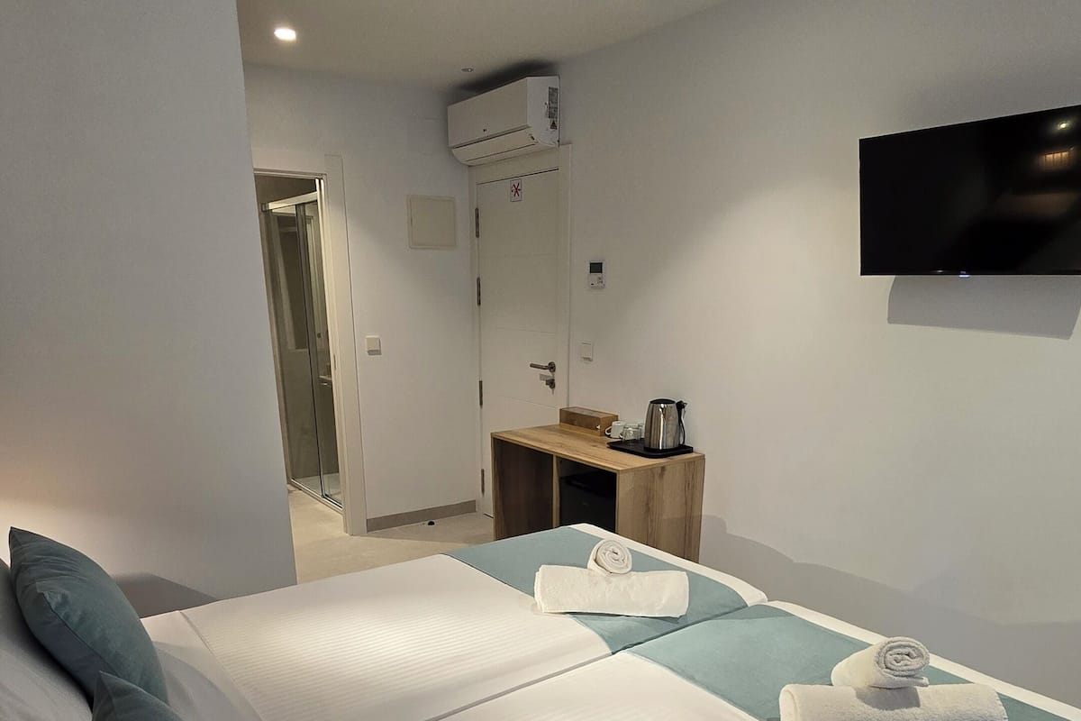 Habitación de hotel con una cama grande, una mesita de noche de madera, un televisor de pantalla plana montado en la pared y un baño visible a través de una puerta abierta.