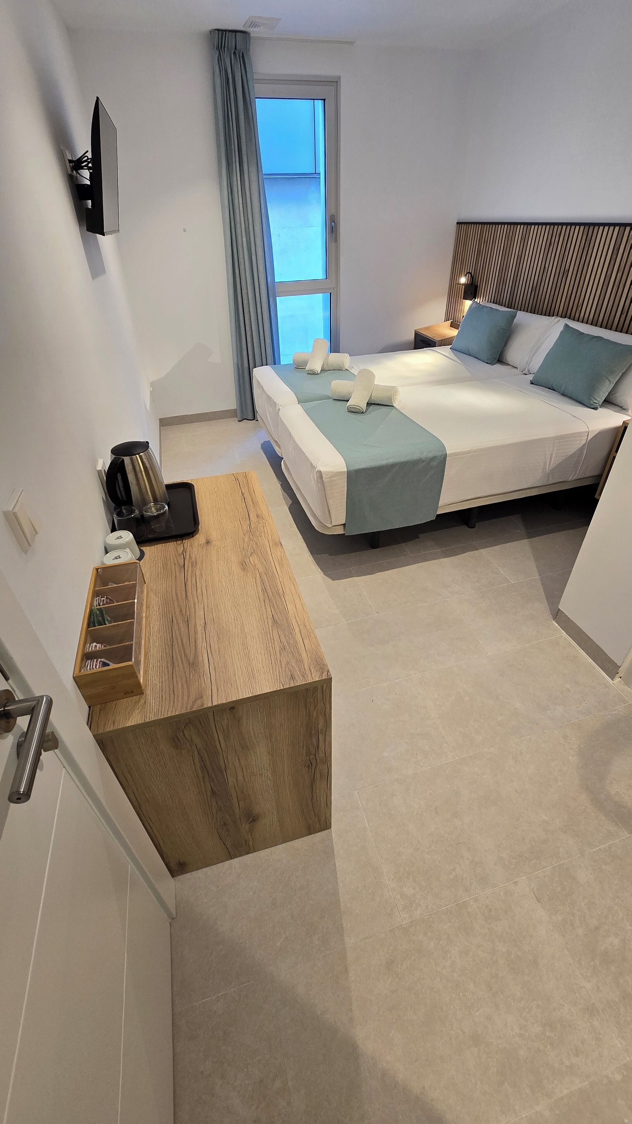 Una habitación de hotel moderna con dos camas, un escritorio de madera, una cafetera y vistas al cielo a través de la ventana.