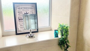 Een badkamer met een wastafel, een lijst met huisregels voor de badkamer, een raam en een potplant.