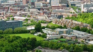 Stadsbeeld met een mix van moderne en traditionele gebouwen, een groot park en een bewolkte lucht.
