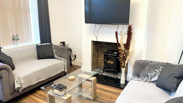 Een moderne woonkamer met een bank, een salontafel, een open haard en een flatscreen televisie aan de muur.
