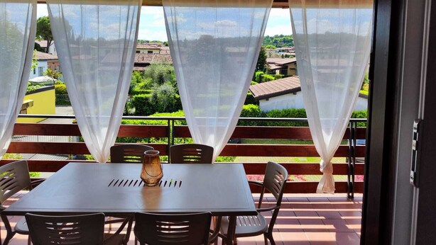 A covered outdoor seating area with a table and chairs, overlooking a residential neighborhood. - Your nest in Manerba (manerba del garda)