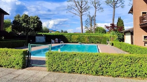 A swimming pool surrounded by well-maintained hedges and trees, with a clear blue sky above. - Your nest in Manerba (manerba del garda)
