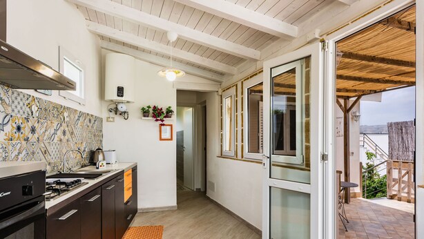 A modern kitchen with dark wooden cabinets, a gas stove, and a tiled backsplash. There is a small window with a view of the outside. - Galatea 4 by Wonderful Italy (Avola)