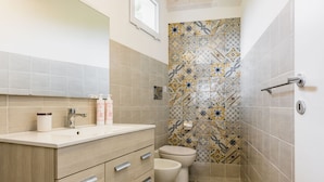 A bathroom with a beige vanity, a toilet, and a shower area with patterned tiles. - Galatea 4 by Wonderful Italy (Avola)