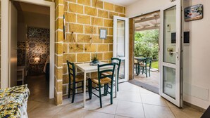 Quarto com parede de pedra, mesa de jantar com cadeiras e vista para o exterior.