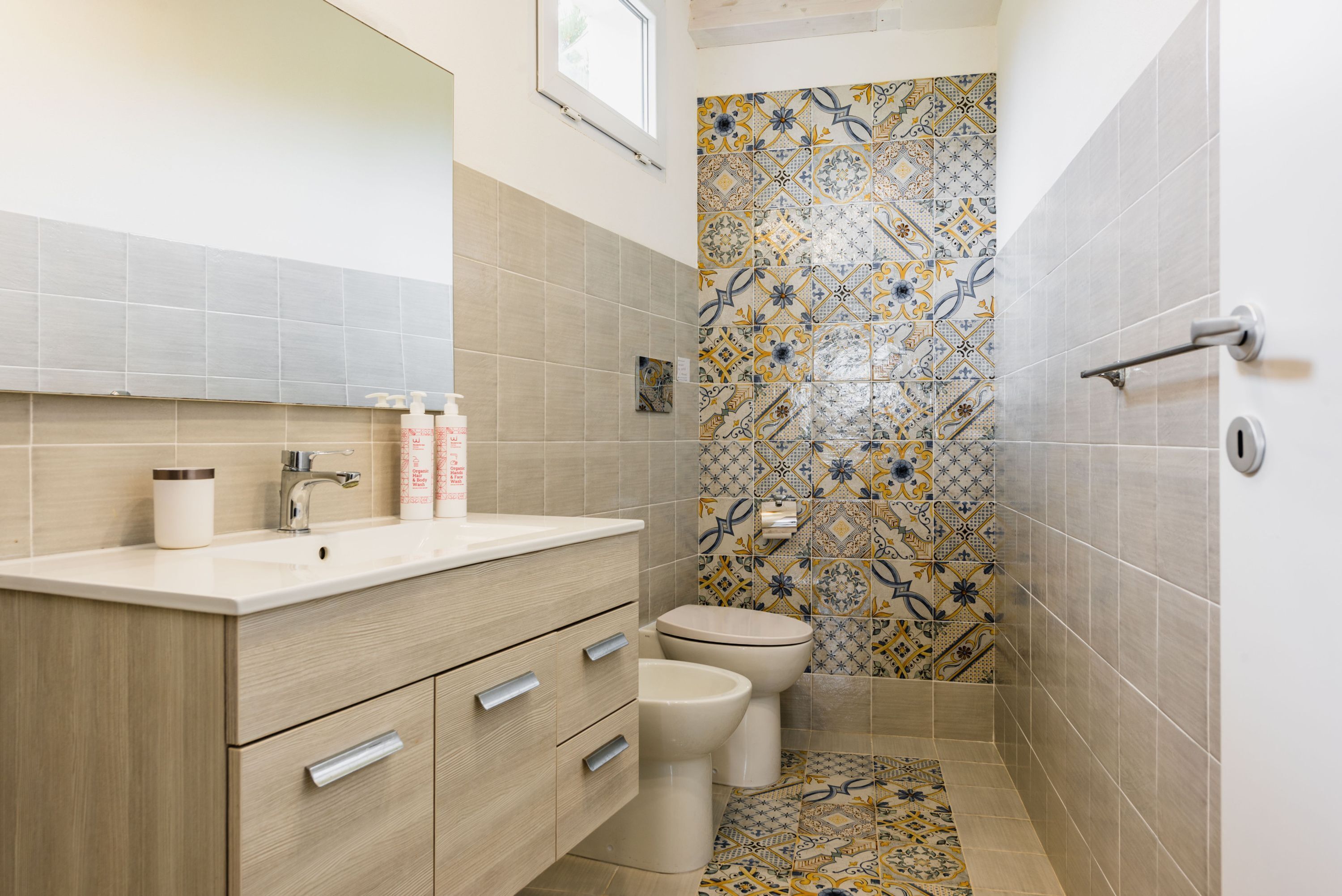A bathroom with a beige vanity, a toilet, and a shower area with patterned tiles.