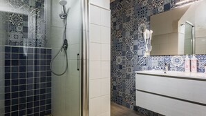 Casa de banho com azulejos estampados, chuveiro e toucador com espelho.