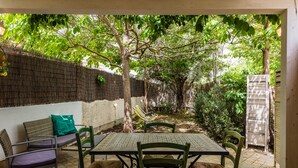 Un patio al aire libre con una mesa y sillas, rodeado por un muro de ladrillo y follaje.