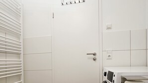 Ein Waschraum mit einer weißen Tür, einer Waschmaschine und einem Wäscheständer.