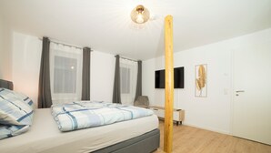 Ein modernes Schlafzimmer mit Bett, Vorhängen, einem an der Wand befestigten Fernseher und einem Holzbalken.