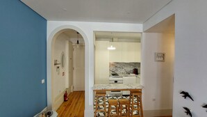 A modern kitchen with white cabinets, a marble countertop, and a built-in oven. There is a small dining area with two stools and a patterned floor. - Downtown Charming by Vacationy (Porto)