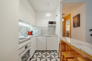 A compact kitchen with white cabinets, a marble countertop, a microwave, and a wooden bench. - Downtown Charming by Vacationy (Porto)