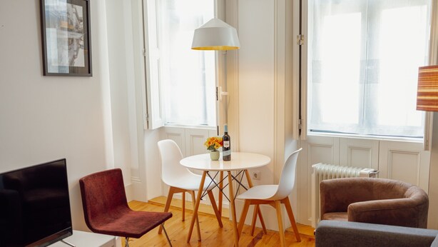 A living room with a TV, a red chair, a grey sofa, a white table with a lamp, and a window with blinds. - Downtown Charming by Vacationy (Porto)