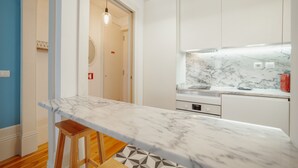 A modern kitchen with white cabinets, a marble countertop, and a wooden stool. - Downtown Charming by Vacationy (Porto)