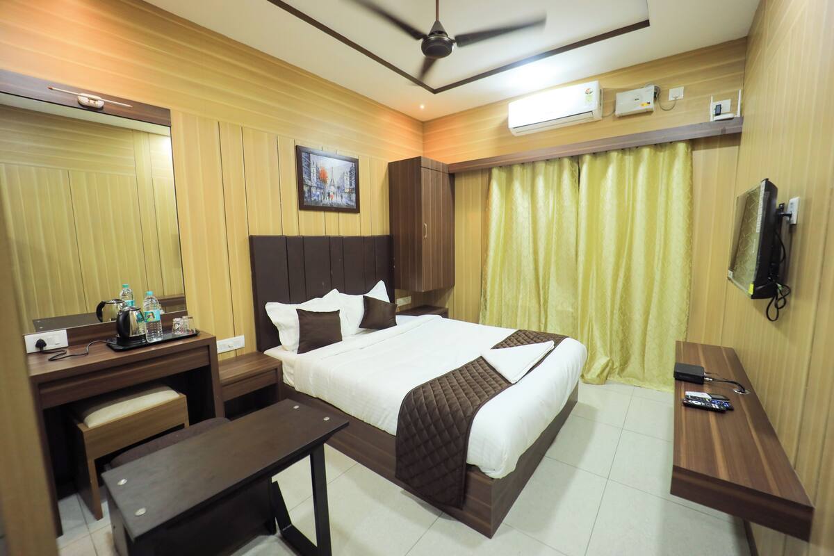 Une chambre d’hôtel avec un grand lit, un bureau avec une chaise, une petite table, un téléviseur et un ventilateur de plafond.