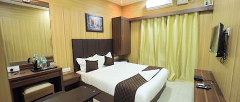 Habitación de hotel con una cama grande, un escritorio con silla, una mesita, un televisor y un ventilador de techo.